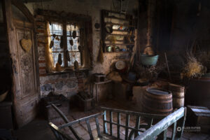 Soba v stari kmečki hiši s polno starimi predmeti, oknom in lesenimi vrati.