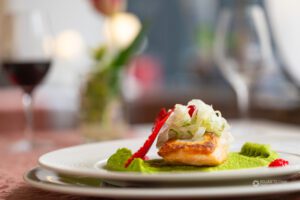 Krožnik z lososom, prilogo in kozarčkom rdečega vina v ozadju